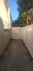 A white privacy fence with a gate installed along a narrow walkway by Miami Fence Installation Contractors in Miami, FL.