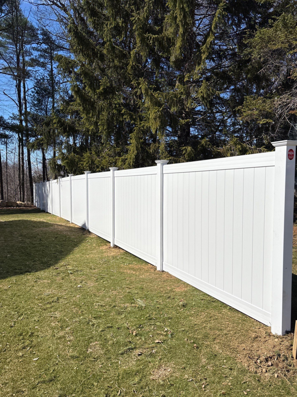A long white privacy vinyl fence installed in a wooded backyard by Vinyl Fences Inc. in Dover, NH.