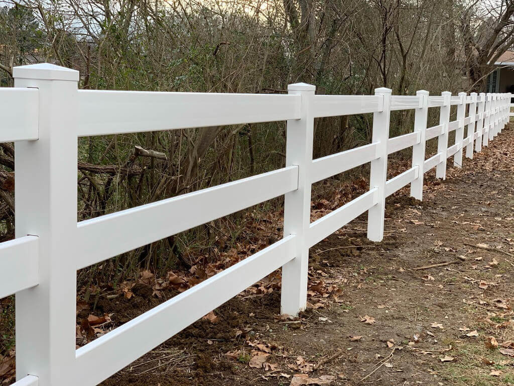 A classic white rail fence bordering a wooded area, installed by Stand Strong Fencing of Plano, TX