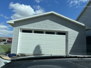 A white residential garage door installed on a light gray house by Tri County Overhead Door Service Inc in New London, WI