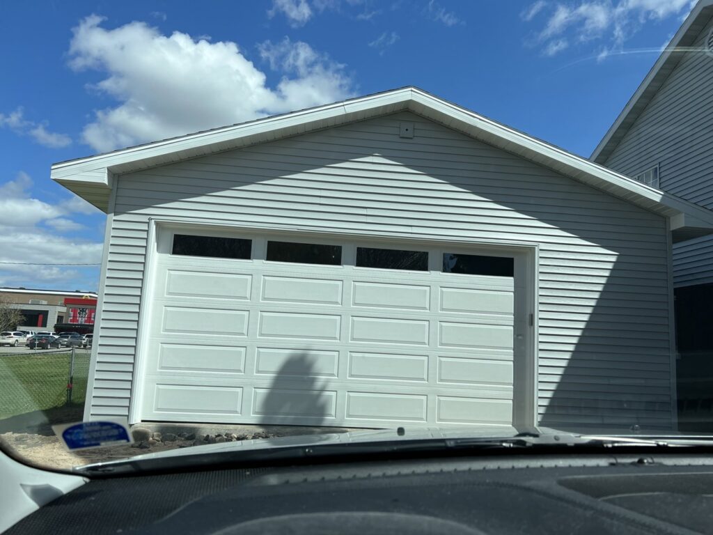 A white residential garage door on a light gray-sided garage, installed by Tri County Overhead Door Service Inc in New London, WI.