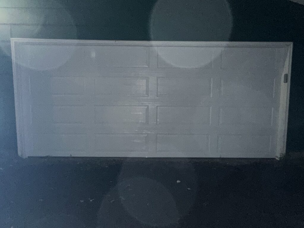 A white residential garage door illuminated at night by AJK Door Services in Duluth, MN.