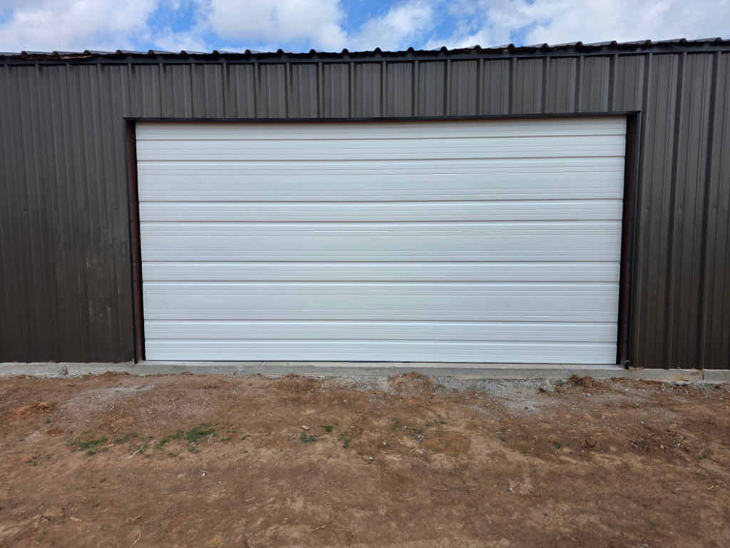 A white roll-up style garage door installed on a metal building by APEX Garage Doors and Carports in Lawton, OK.