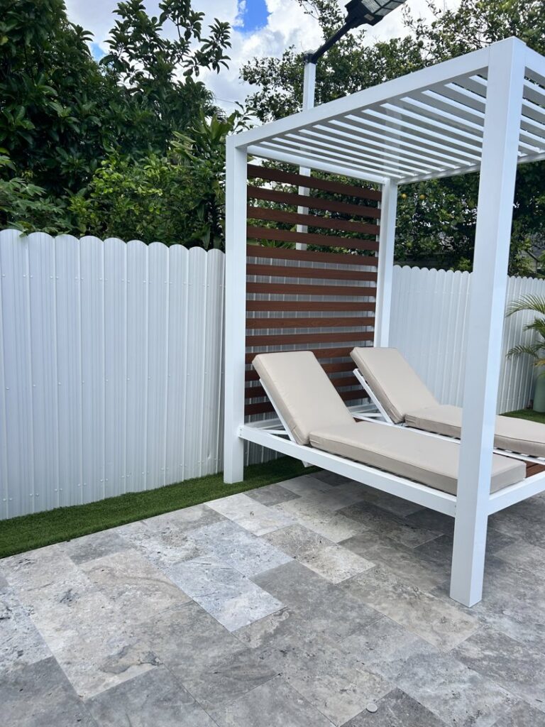 A white scalloped metal privacy fence installed next to a modern pergola by Osuna Ornamental Fences & Gates in Cutler Bay, FL.