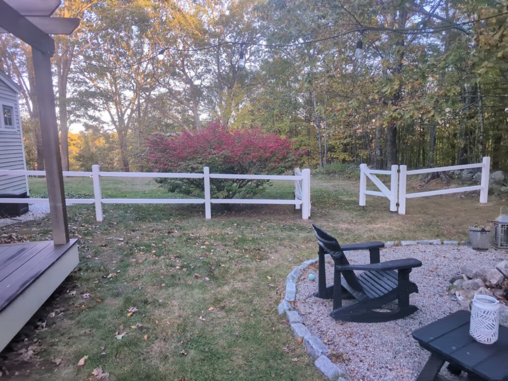 A charming white split-rail fence with a gate defining a backyard space by Precision Fence NH in Hooksett, NH.