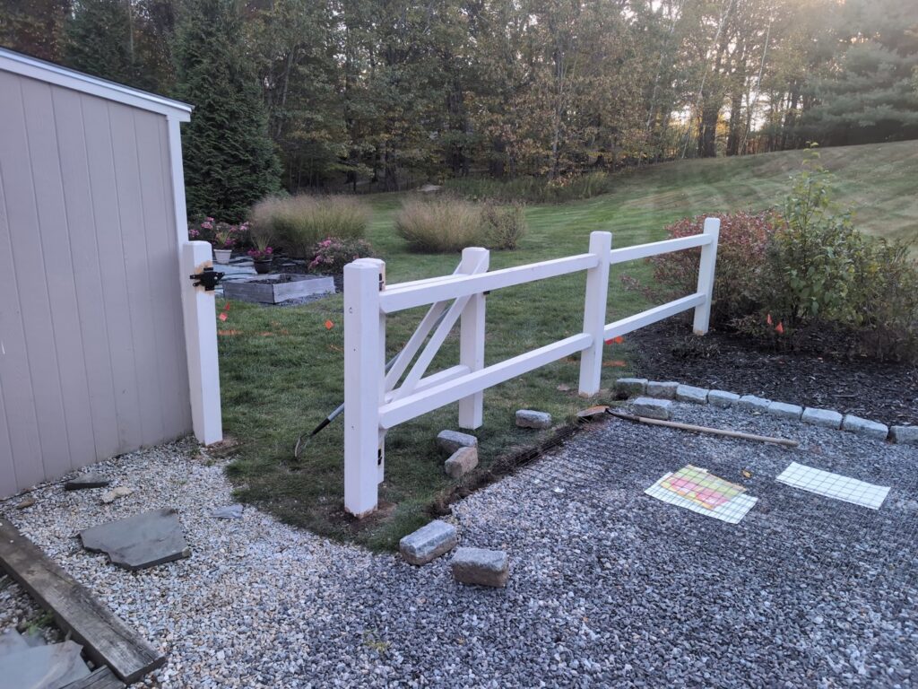 A white split-rail fence with a gate being installed next to a shed by Precision Fence NH in Hooksett, NH.