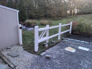 A white split-rail fence with a gate being installed next to a shed by Precision Fence NH in Hooksett, NH.