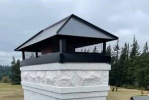 A white stone chimney with a new black metal cap installed by Professional Fireplaces and Chimney Sweeps in Huntsville, AL.