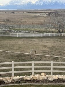 A white three-rail vinyl farm fence installed in a rural setting with mountains by All American Vinyl in Provo, UT.