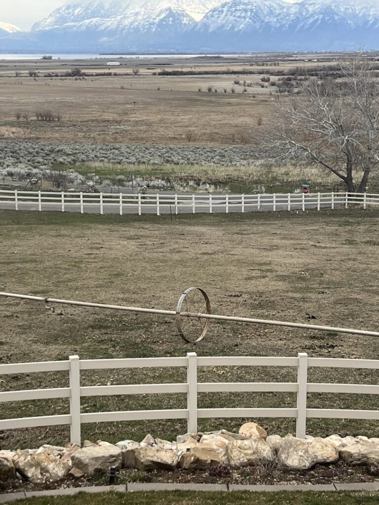 A white three-rail vinyl farm fence installed in a rural setting with mountains by All American Vinyl in Provo, UT.