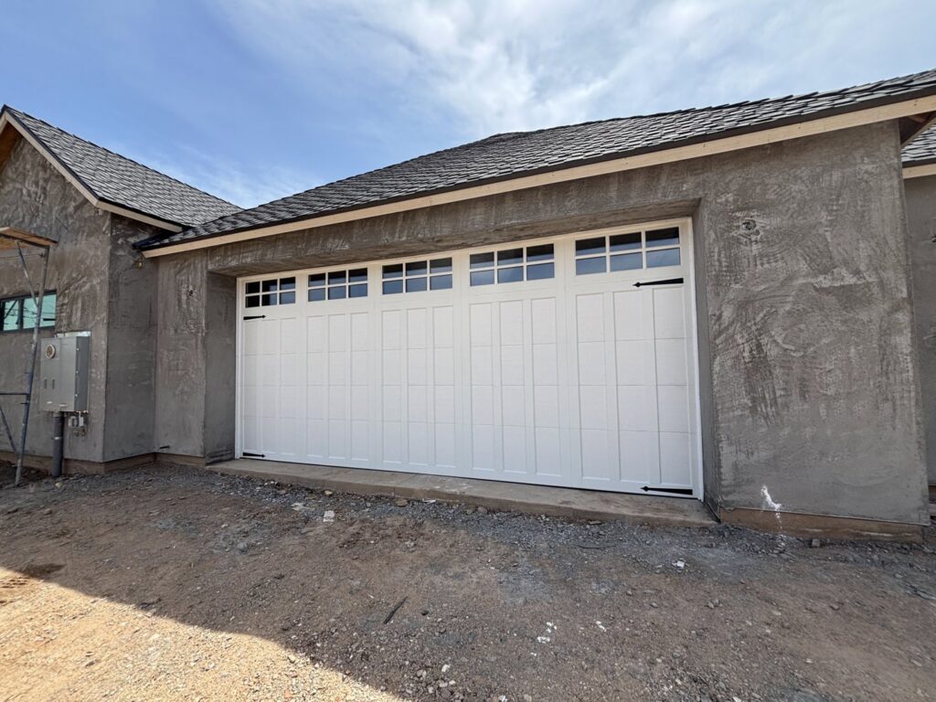 A white traditional style garage door with top windows installed on a new construction home by Stapley Action Garage Door in Mesa, AZ.