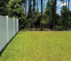 A white vinyl privacy fence and a black metal fence installed in a residential backyard by Barwick Fence Company in Savannah, GA.