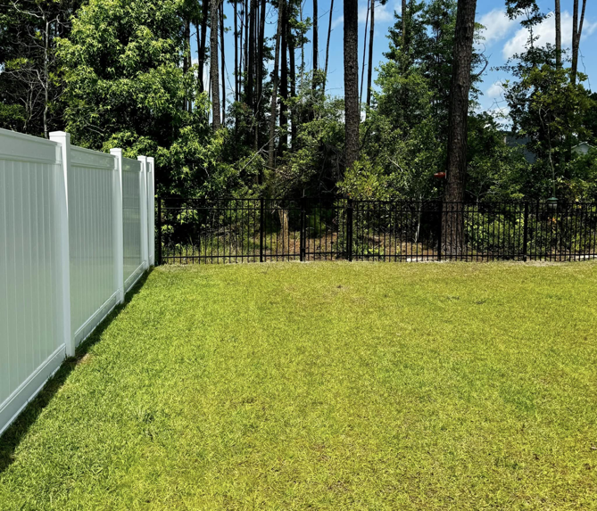 A white vinyl privacy fence and a black metal fence installed in a residential backyard by Barwick Fence Company in Savannah, GA.