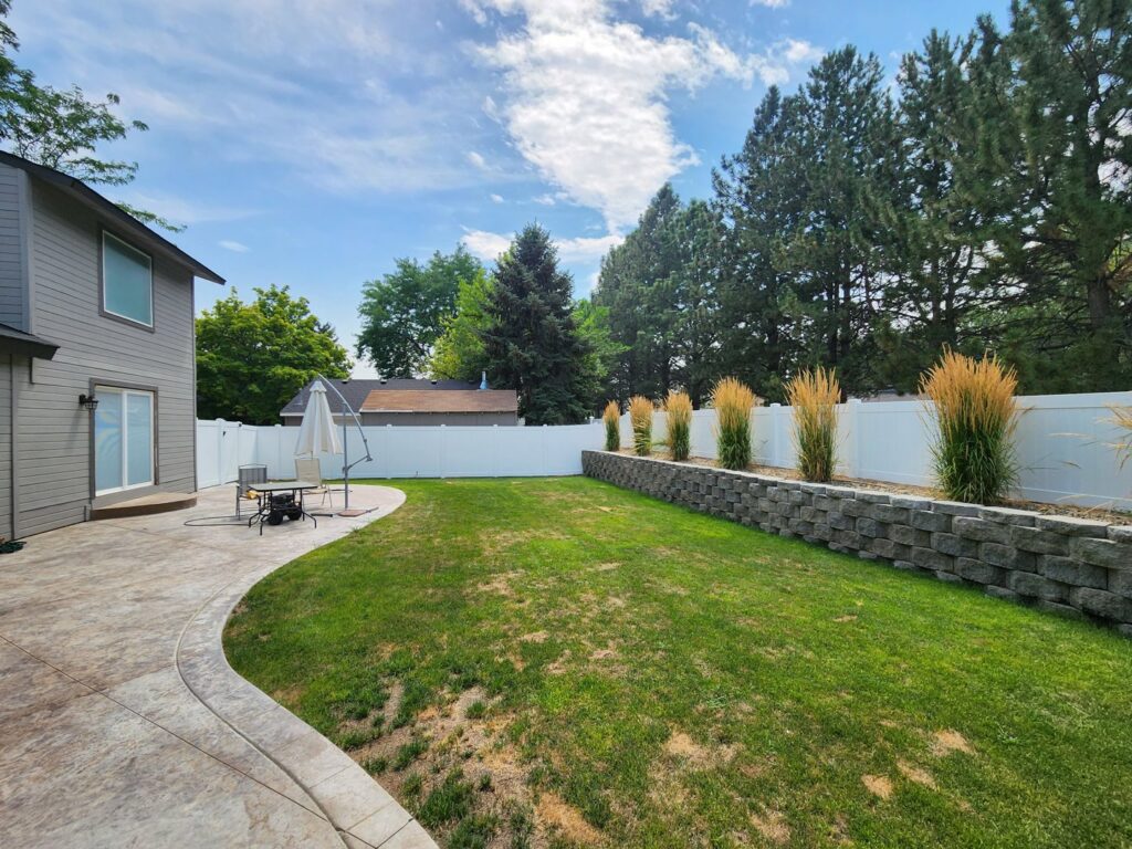 A white vinyl fence installed in a landscaped backyard with a retaining wall by Josey's Fencing LLC in Caldwell, ID.