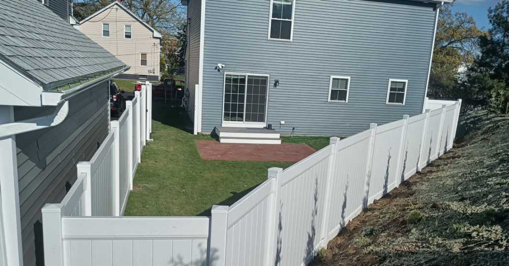 A newly installed white vinyl fence enclosing a backyard at a residential property by Ocean State Fence Works LLC in North Kingstown, RI.