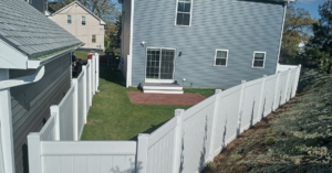 A newly installed white vinyl fence enclosing a backyard at a residential property by Ocean State Fence Works LLC in North Kingstown, RI.