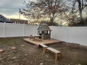 A white vinyl fence enclosing a backyard with a playhouse installed by Pride Fence in Peabody, MA.