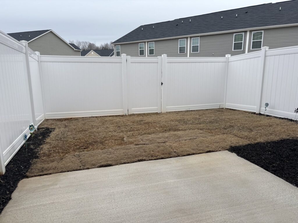 A white vinyl privacy fence enclosing a backyard with a gate, installed by Outsiders Fencing in Greensboro, NC.