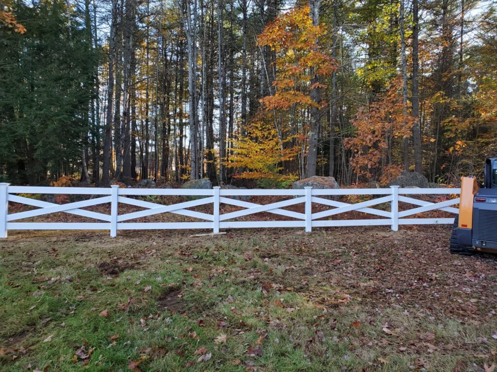A white vinyl cross-buck style fence installed along a property line by MH Fence in Weare, NH.