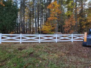 A white vinyl cross-buck style fence installed along a property line by MH Fence in Weare, NH.