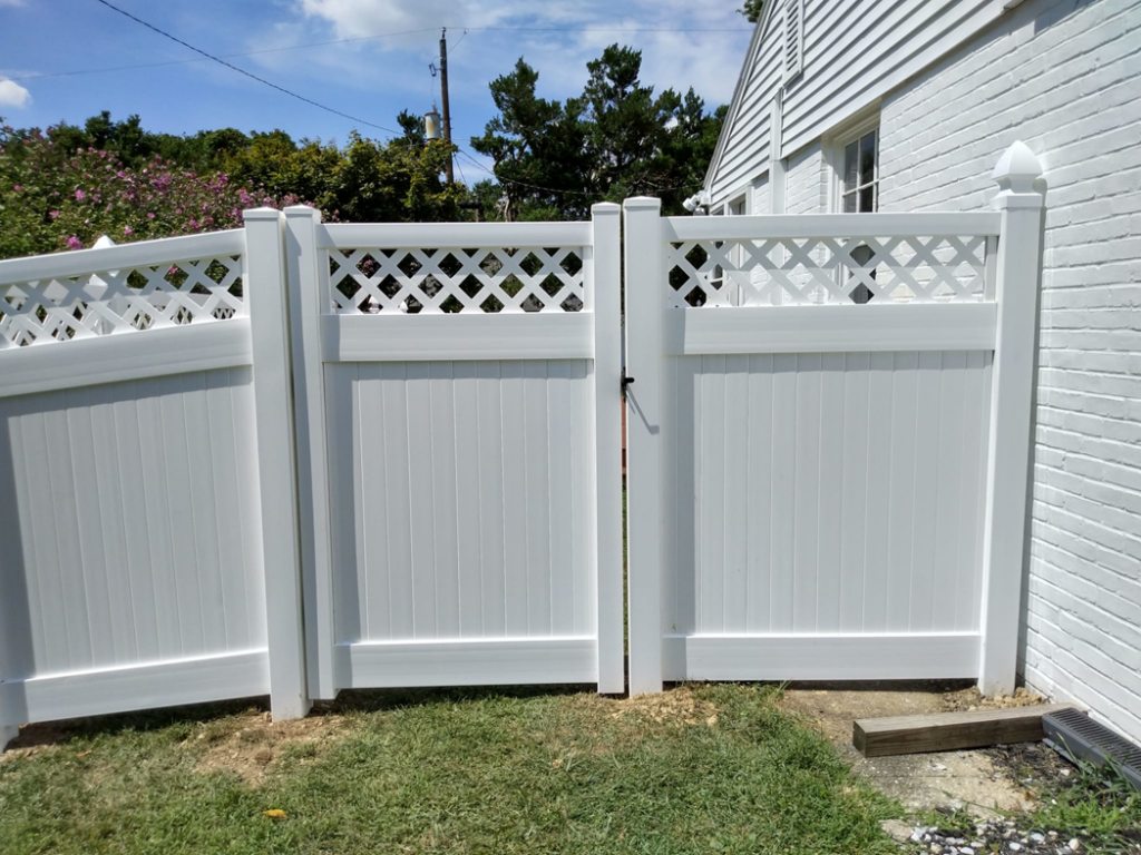 A white vinyl double gate with decorative lattice tops installed next to a white brick house by Low-Level Construction LLC in York, PA.