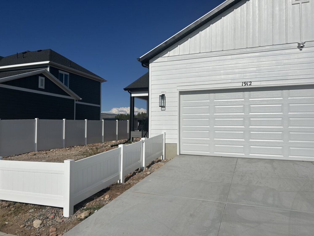 A new white vinyl fence installed along a driveway by Stonehenge Fence & Deck in Orem, UT.