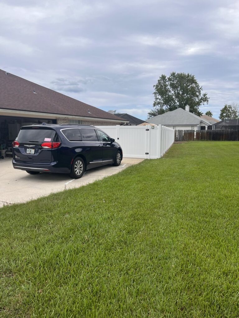 A white vinyl privacy fence extending along a driveway, offering seclusion and style by Exacta FENCE LLC in Jacksonville, FL.