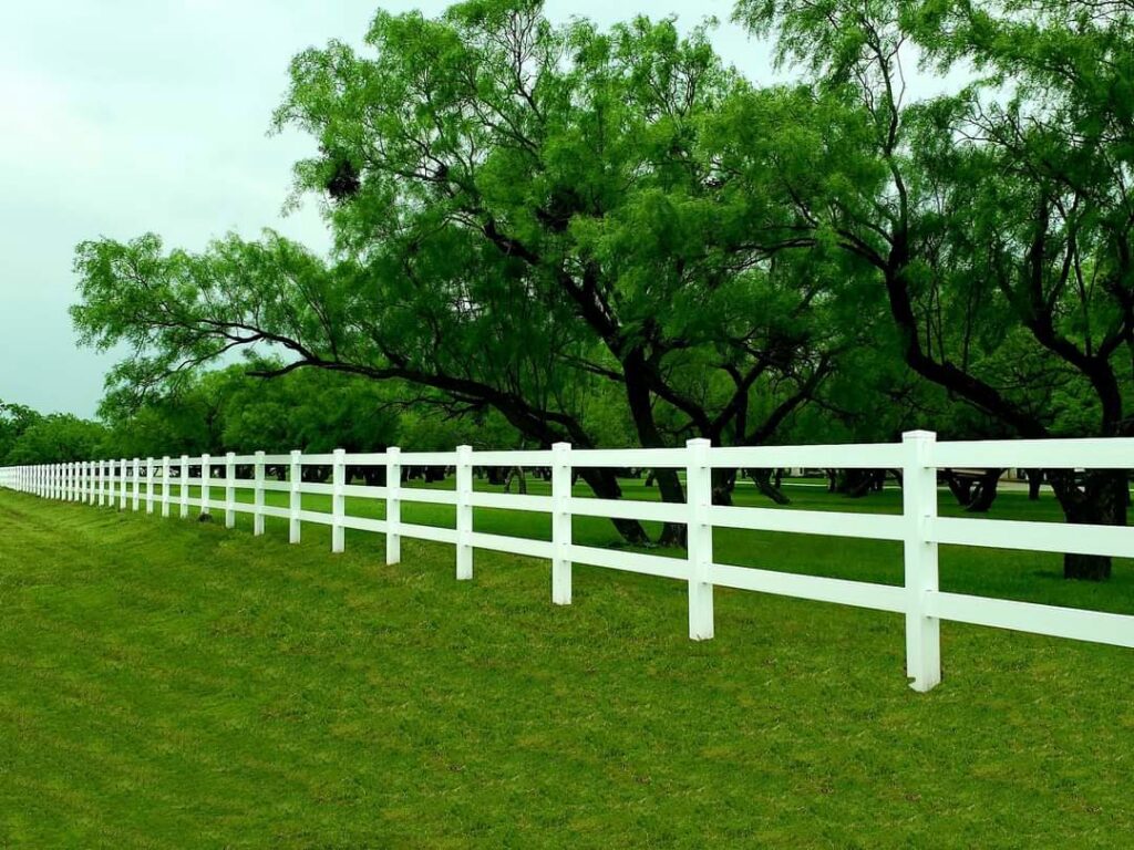 A scenic white vinyl farm fence stretching across a green landscape by Pro Insulation and Fence in Wichita Falls, TX.