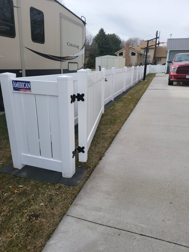 A white vinyl fence installed along a residential driveway next to an RV by American Fence Company of Norfolk in Grand Island, NE.