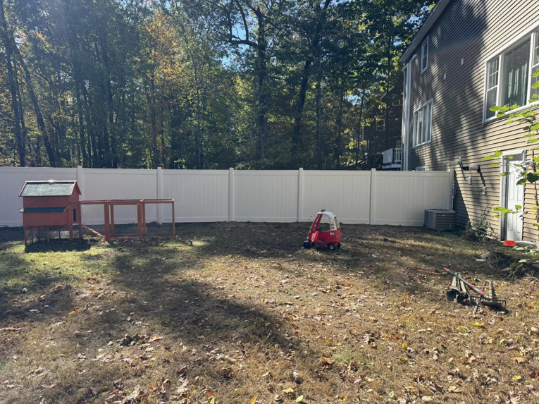 A long white vinyl fence installed along the back of a house in a residential backyard by David Platania Fence in Derry, NH.