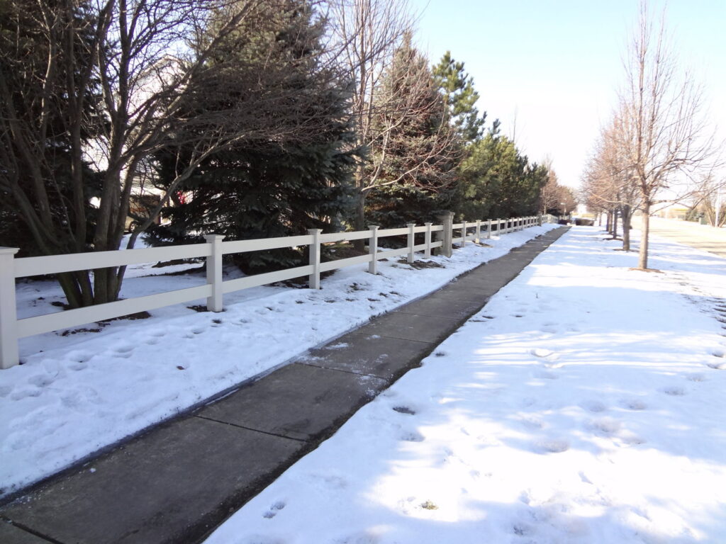A white vinyl fence installed along a sidewalk in a snowy landscape by Fence Connection, Inc. in Elgin, IL.