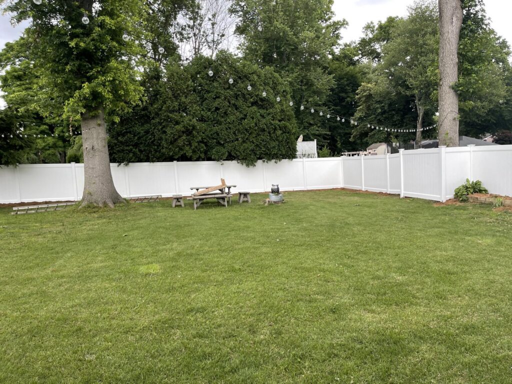 A white vinyl fence enclosing a spacious backyard with mature trees, installed by Brothers Fence in Elizabeth, NJ.