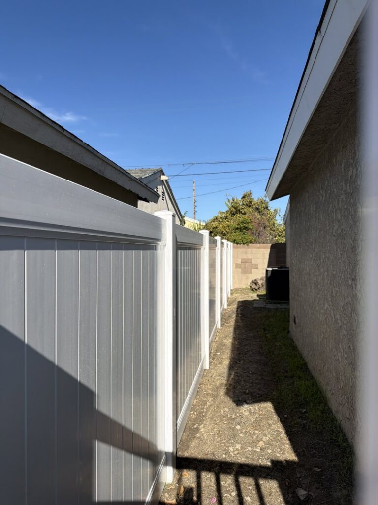 A white vinyl privacy fence installed along a narrow pathway between two residential homes by True American Fence Supply and Construction in Anaheim, CA.