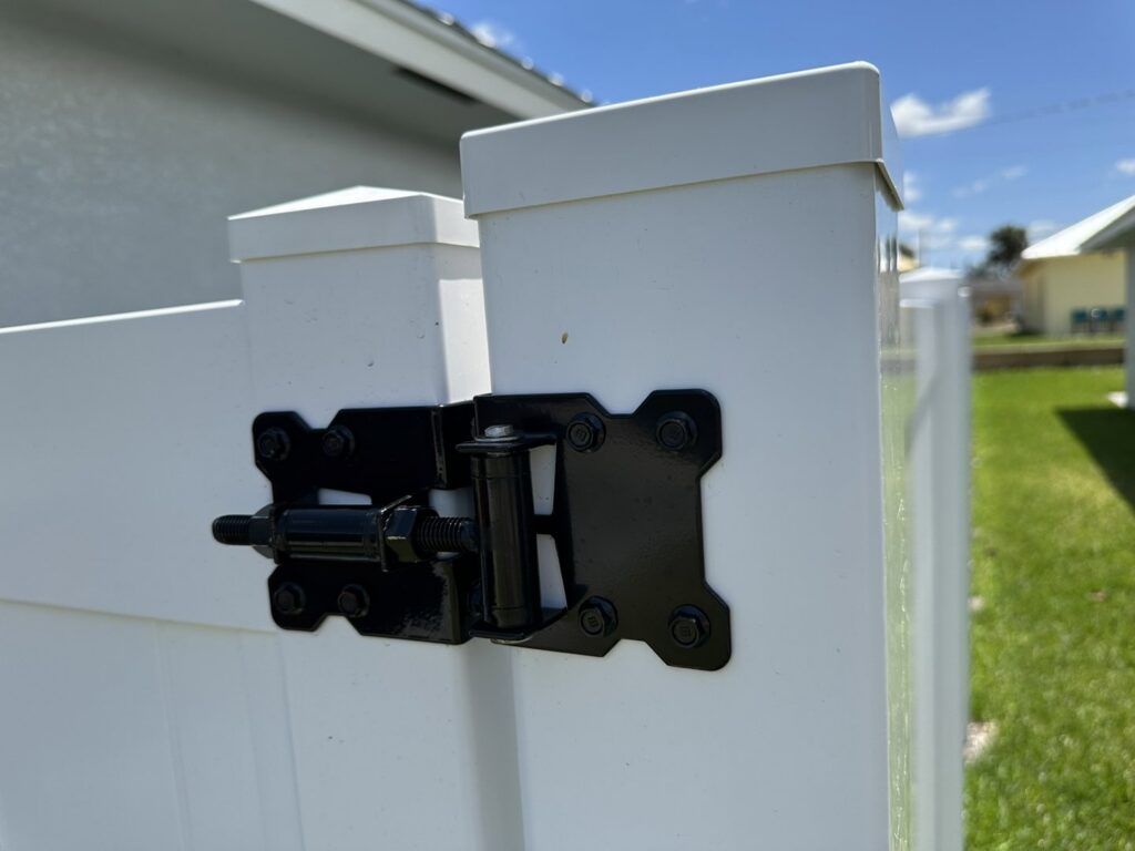 A close-up view of a durable black hinge on a white vinyl fence gate, installed by Inovation Fence in Fort Worth, TX.