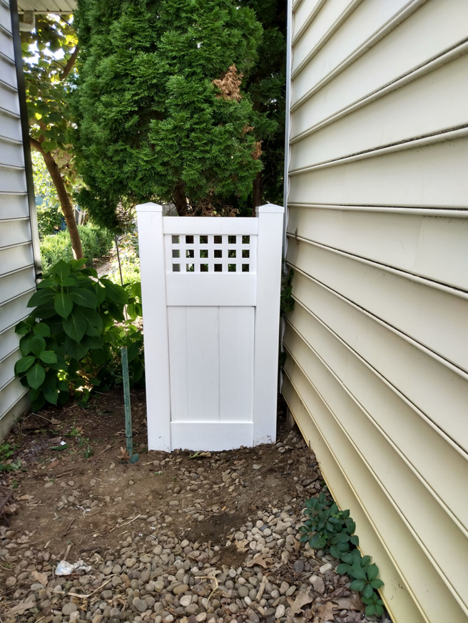 A white vinyl fence gate with a lattice top installed between a house and dense landscaping by Low-Level Construction LLC in York, PA.