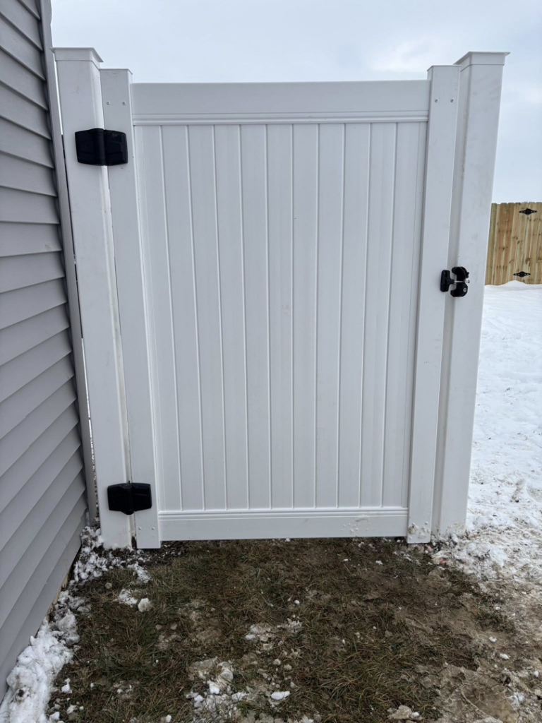 A newly installed white vinyl fence gate next to a residential home by H&M Fencing LLC in Decatur, IN.