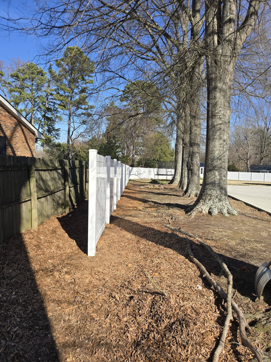 A white vinyl fence installed alongside an existing wooden fence by Outsiders Fencing in Greensboro, NC.
