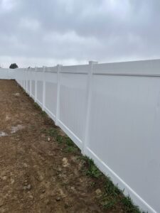 A newly installed white vinyl privacy fence along a property line in a new construction area by RDU Fence in Holly Springs, NC.