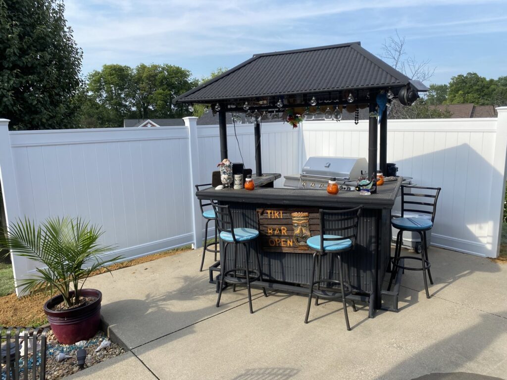 A white vinyl fence enclosing a patio area with an outdoor tiki bar by Nailed It Fencing and Exteriors in Evansville, IN.