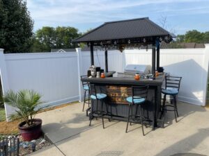 A white vinyl fence enclosing a patio area with an outdoor tiki bar by Nailed It Fencing and Exteriors in Evansville, IN.