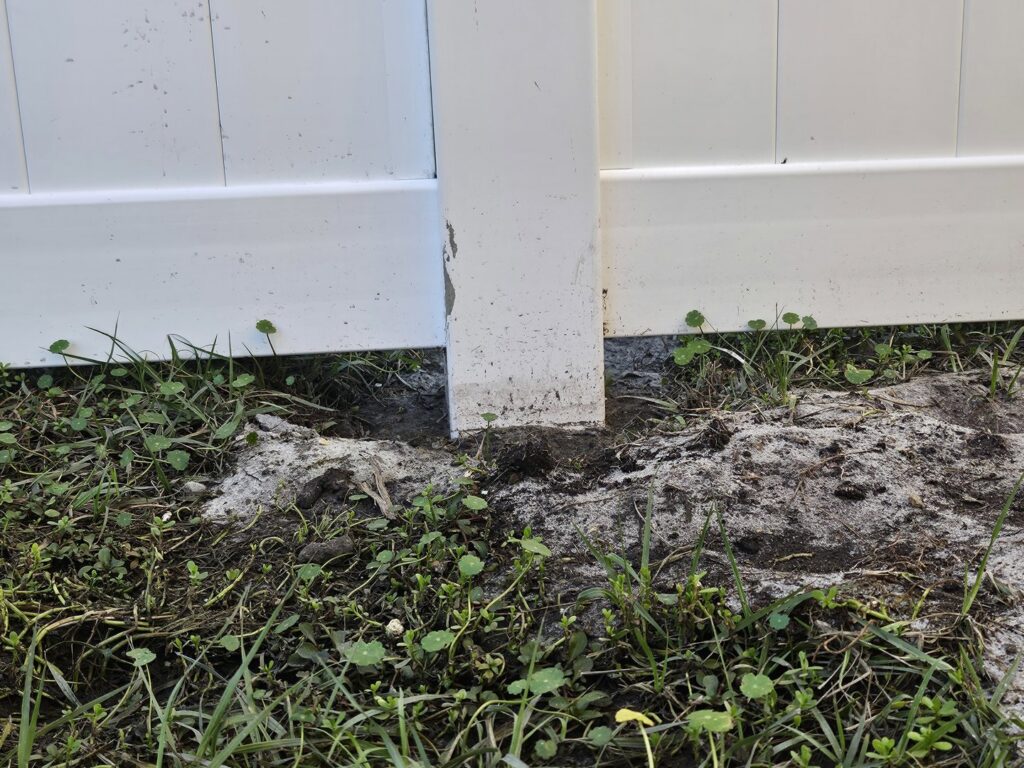 Close-up of a white vinyl fence post base firmly set in the ground by R&R Fence Services in Jacksonville, FL.