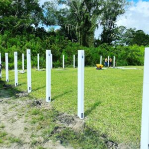 Workers installing white vinyl fence posts in a grassy field for Top Fence LLC in Jacksonville, FL.