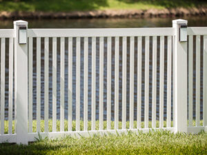 A white vinyl fence with decorative solar post caps installed near a body of water by Superior Fence & Rail of Charlotte, NC