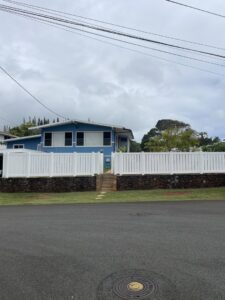 A white vinyl fence with a gate built on a decorative stone wall in front of a house by Redmond Valleywide - Hawaii's Fence Company in Kapolei, HI
