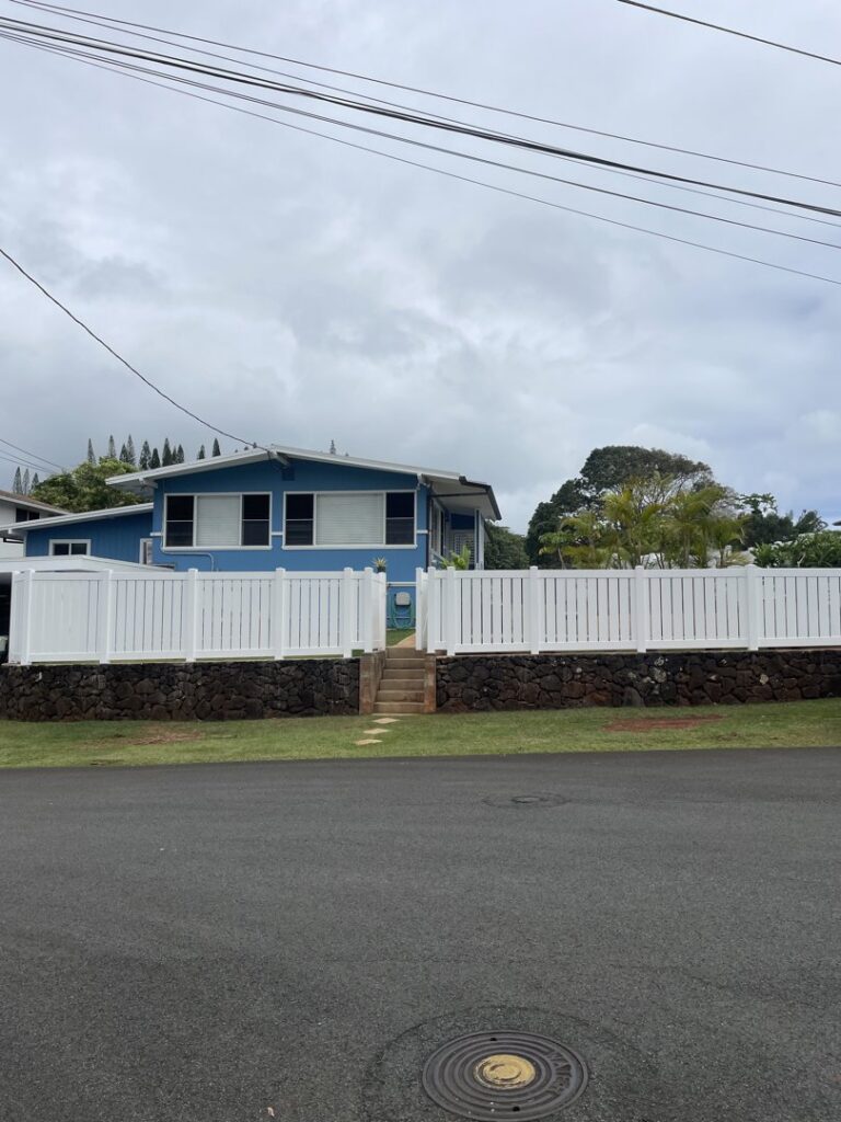 A white vinyl fence with a gate built on a decorative stone wall in front of a house by Redmond Valleywide - Hawaii's Fence Company in Kapolei, HI