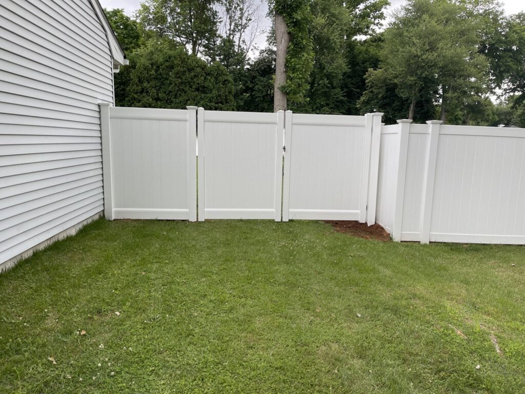 A newly installed white vinyl fence with two gates in a residential yard by Brothers Fence in Elizabeth, NJ.