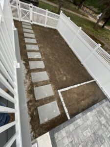 A white vinyl fence with a gate surrounding a backyard with new stepping stones and patio by OMA Fence,LLC in Weymouth, MA