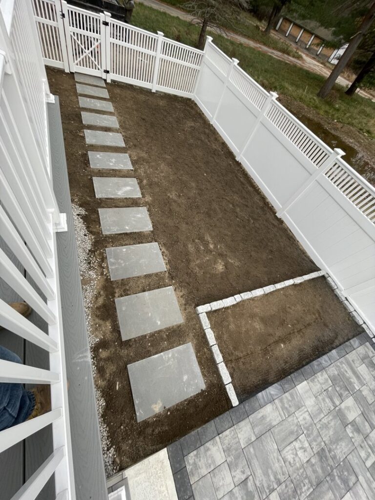 A white vinyl fence with a gate surrounding a backyard with new stepping stones and patio by OMA Fence,LLC in Weymouth, MA
