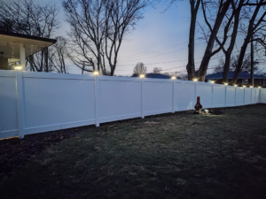 A long white vinyl fence with illuminated post caps at dusk, installed by Fence Guys INC in Cleveland, OH.