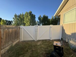 A white vinyl gate with a diagonal brace design installed next to an existing wood fence by 208 Fence and Gate in Idaho Falls, ID.